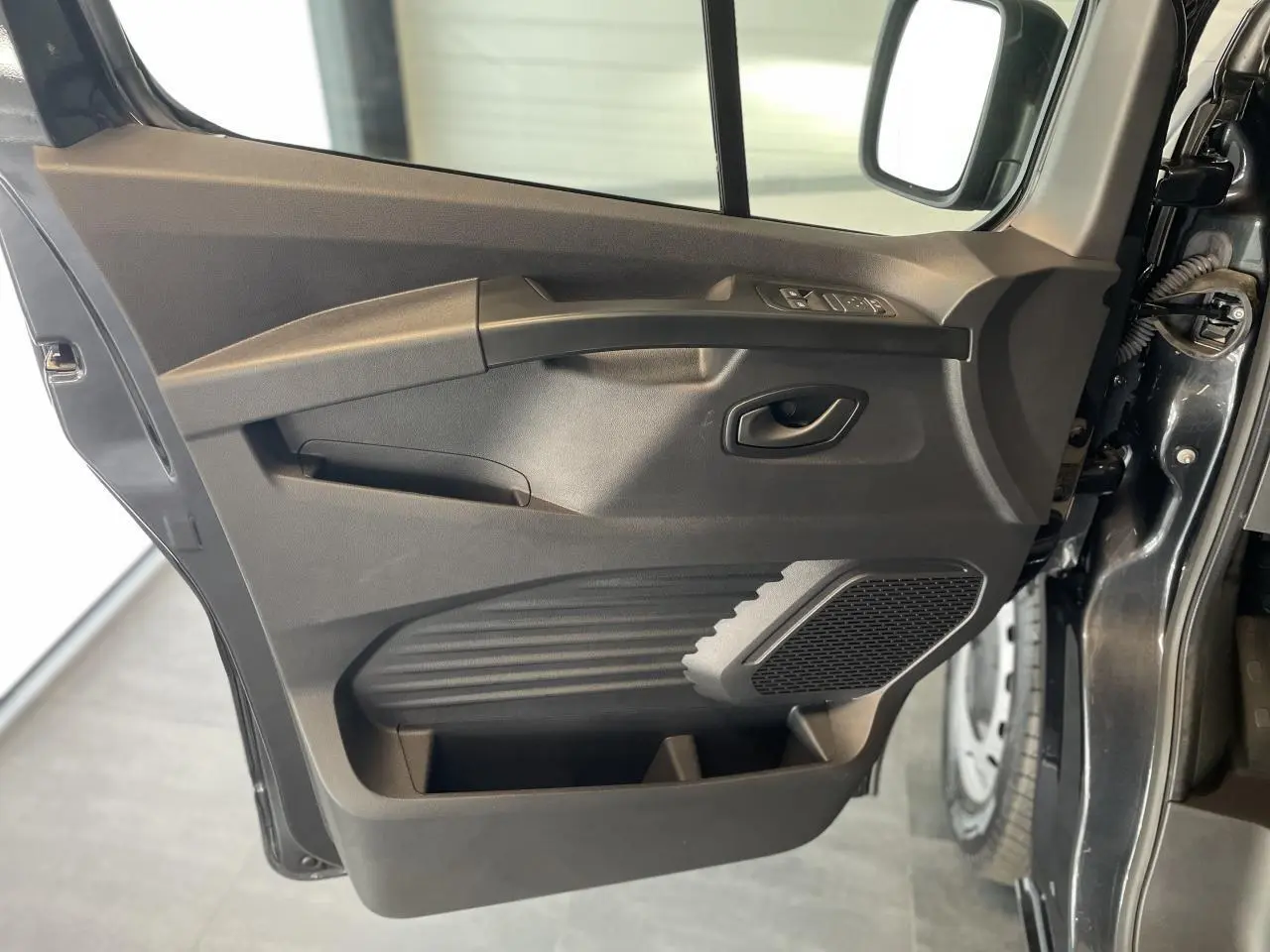Vue rapprochée de la porte avant gauche gris comète du Renault Trafic Fourgon, avec commandes de vitres et haut-parleur intégré.