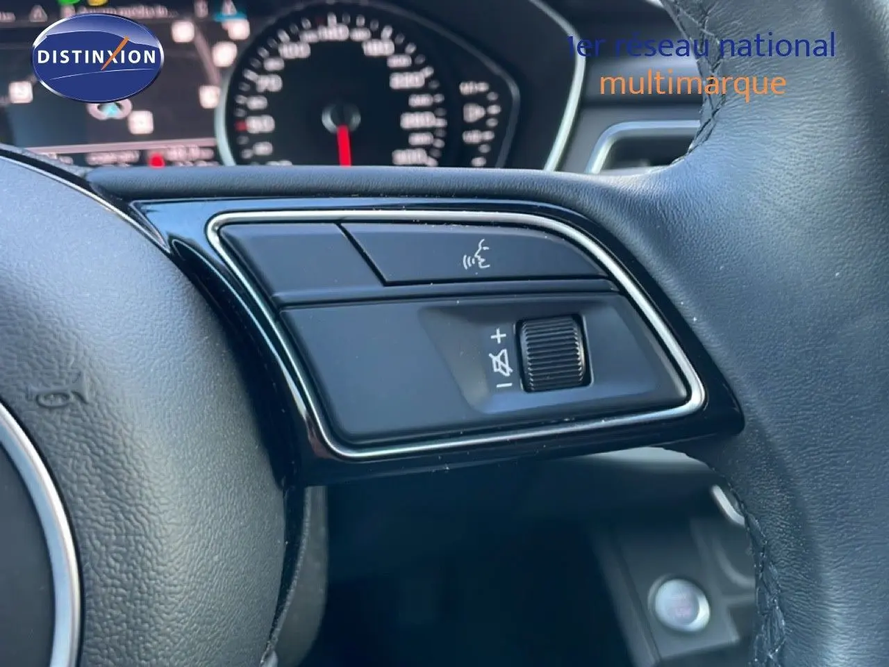 Gros plan sur les commandes vocales et volume au volant cuir d'une Audi A4 Avant gris Manhattan, tableau de bord flou en arrière-plan.