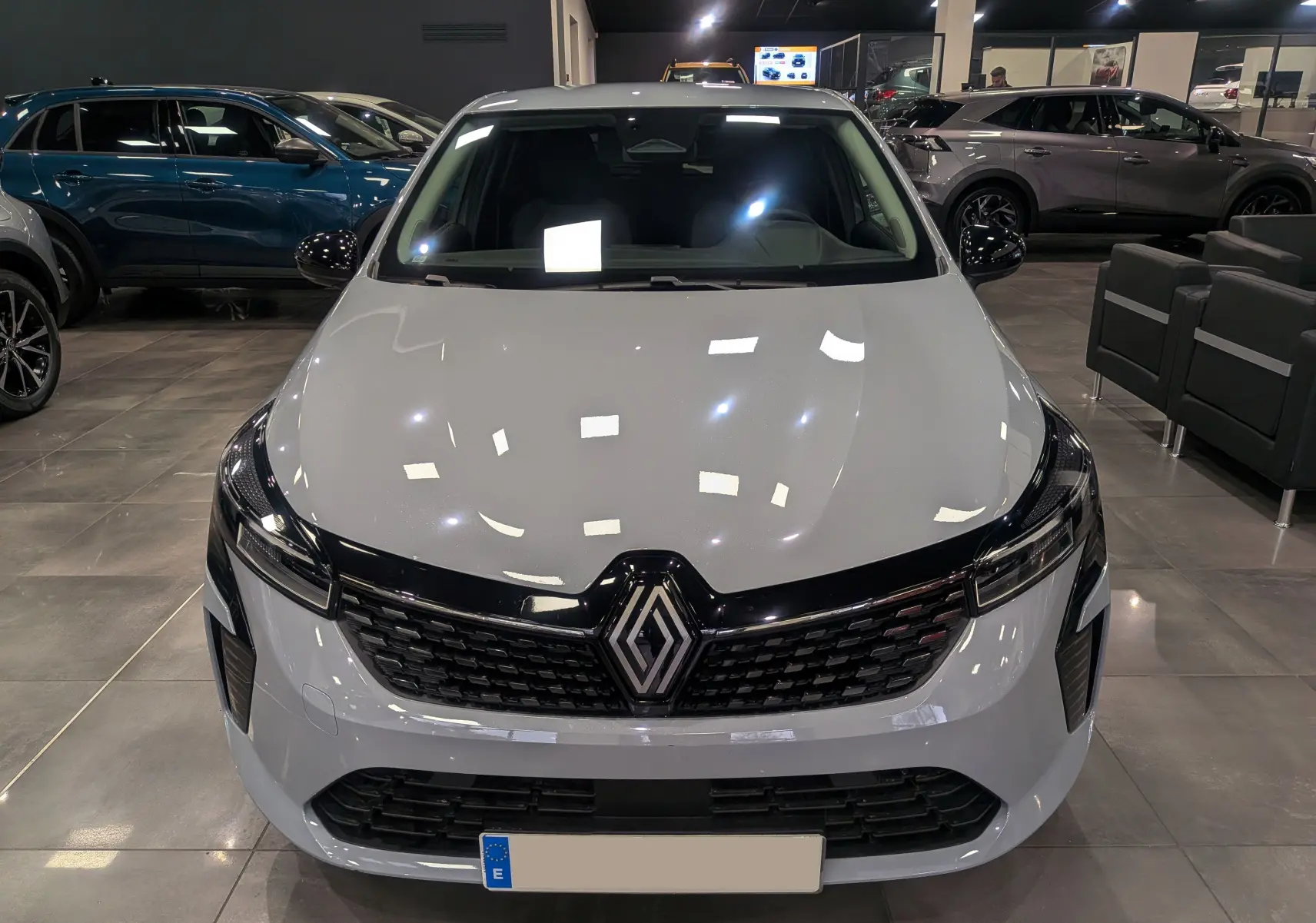 Vue frontale d'une Renault Clio V gris Rafale en showroom, avec calandre noire et logo Renault bien visible.