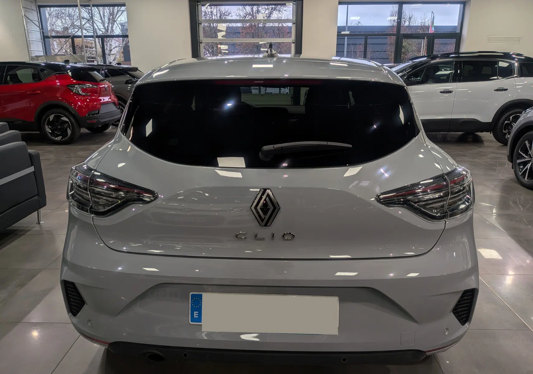 Vue arrière d'une Renault Clio V gris Rafale en intérieur, soulignant ses feux arrière LED et son logo central chromé.