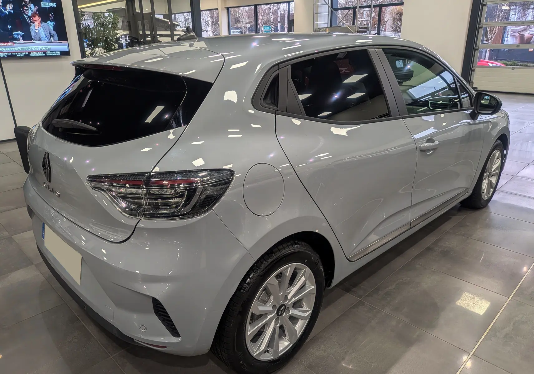 Vue 3/4 arrière droite d'une Renault Clio V gris Rafale en showroom, soulignant ses feux arrière LED et jantes alliage.