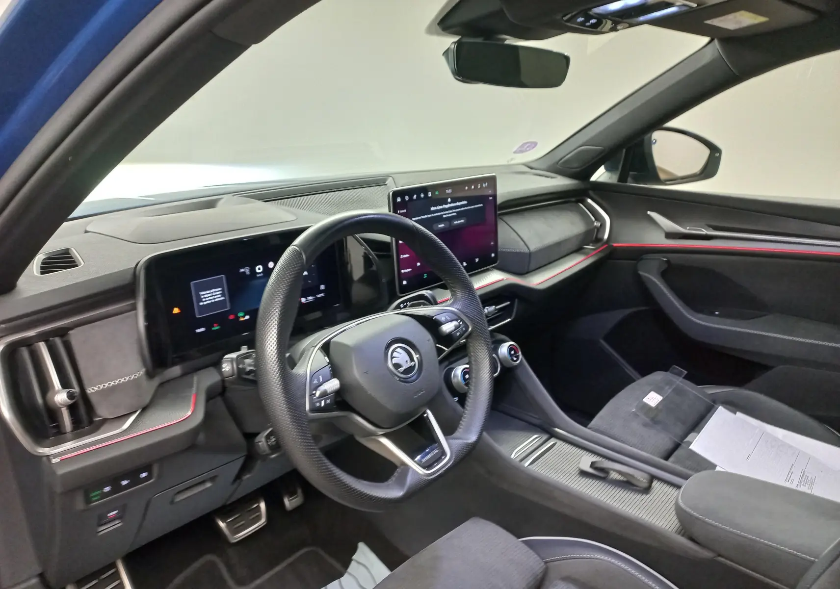 Vue intérieure côté conducteur du Skoda Kodiaq 2024 Sportline, tableau de bord moderne avec écran tactile et éclairage d’ambiance rouge.