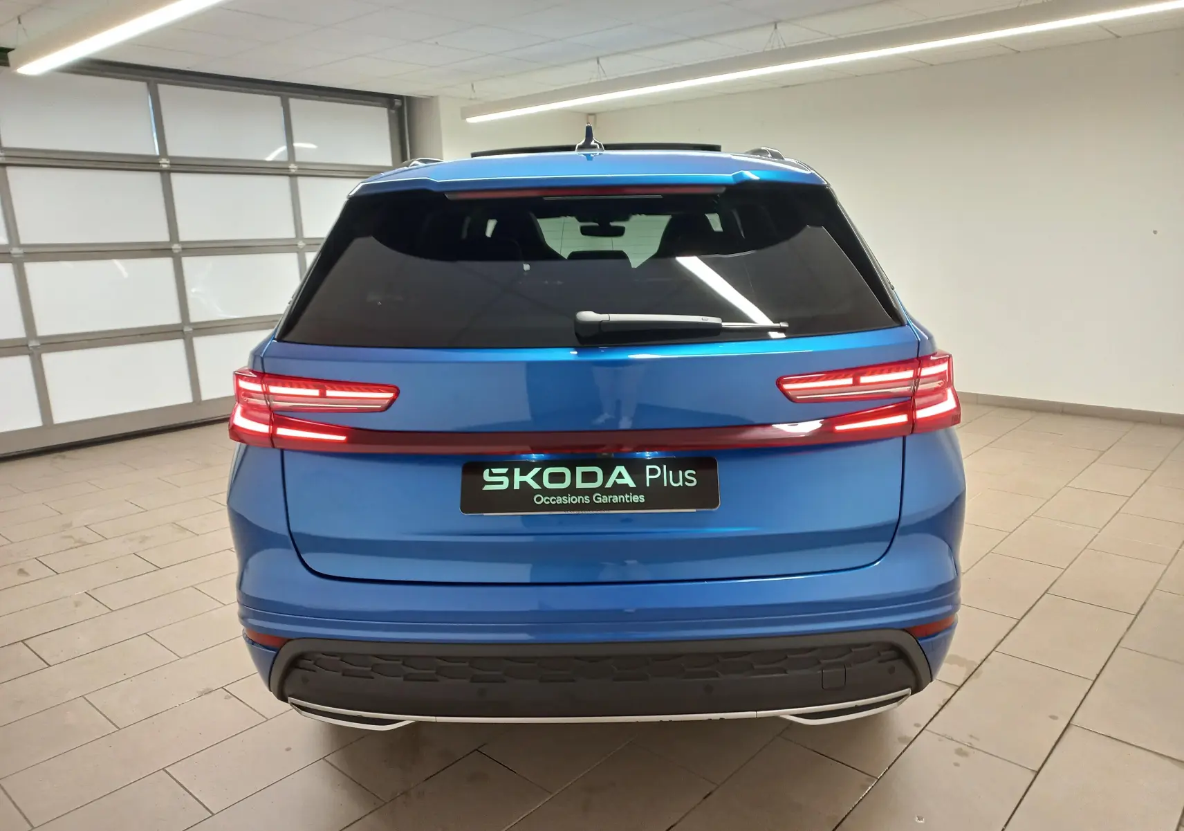 Vue arrière du Skoda Kodiaq 2024 Bleu RS avec feux LED reliés par un bandeau lumineux rouge dans un garage.