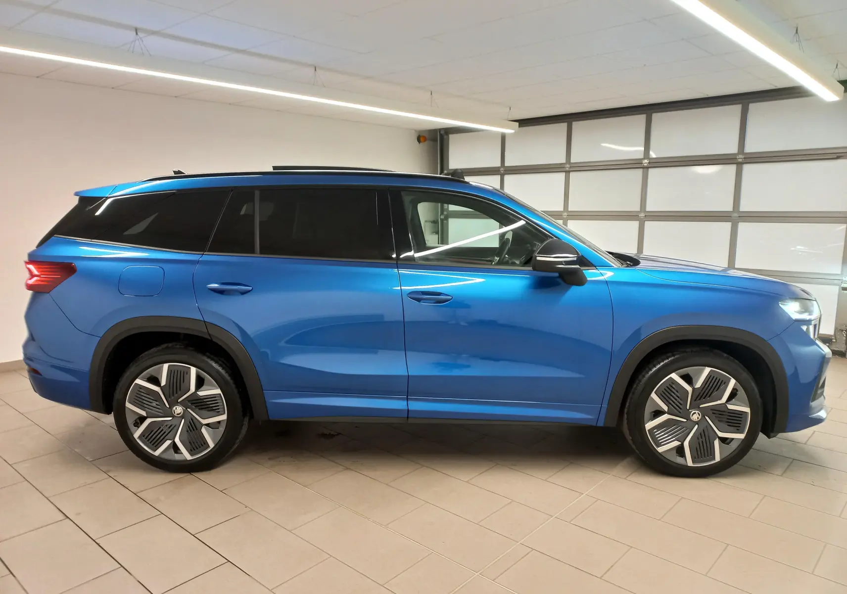 Vue de profil côté gauche d'un Skoda Kodiaq 2024 bleu RS avec jantes alliage 20 pouces et toit panoramique.