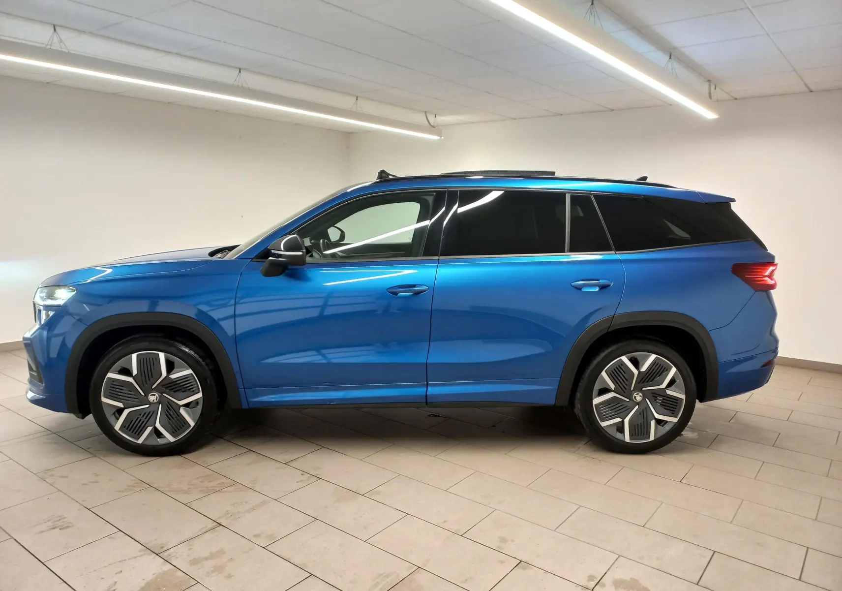 Vue de profil côté gauche d'un Skoda Kodiaq 2024 bleu RS avec jantes alliage 20'' Rila anthracite et toit panoramique.
