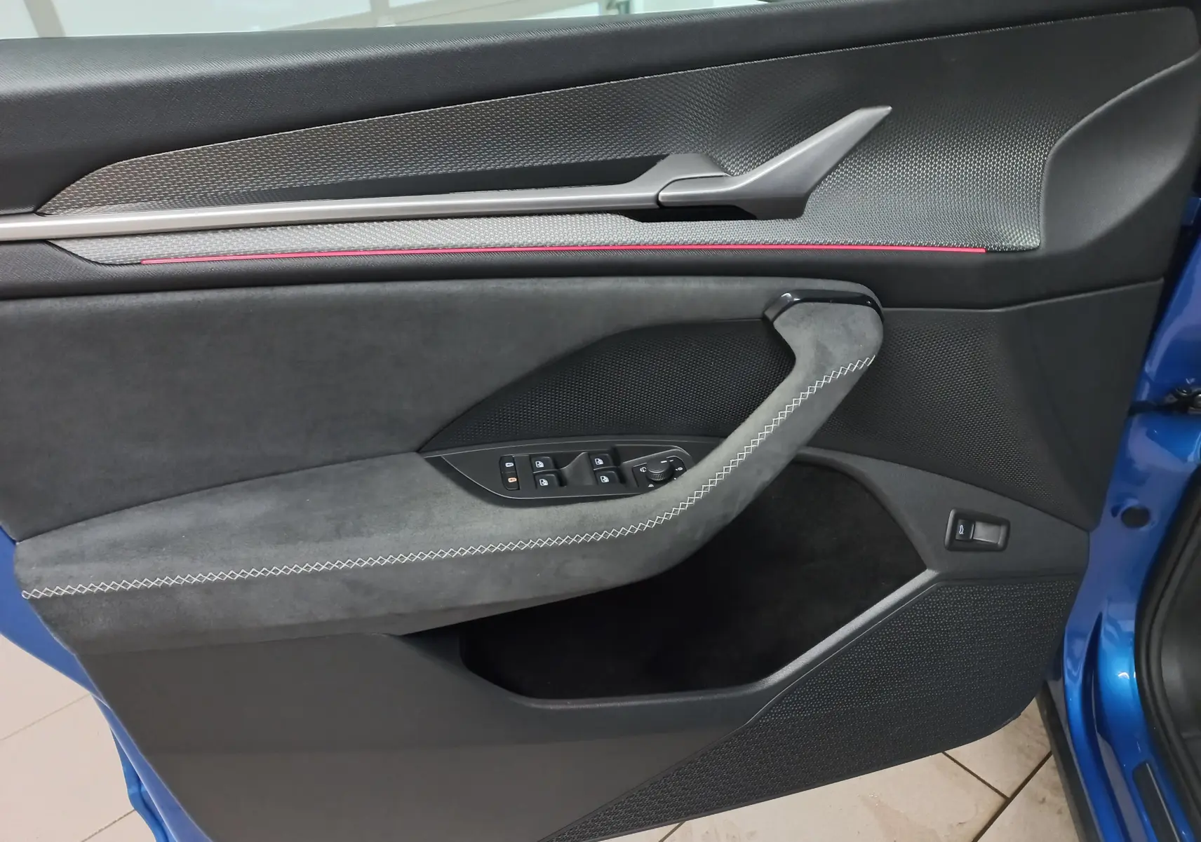 Vue intérieure côté gauche de la porte avant d’un Skoda Kodiaq Bleu RS 2024 avec garniture noire et surpiqûres blanches.