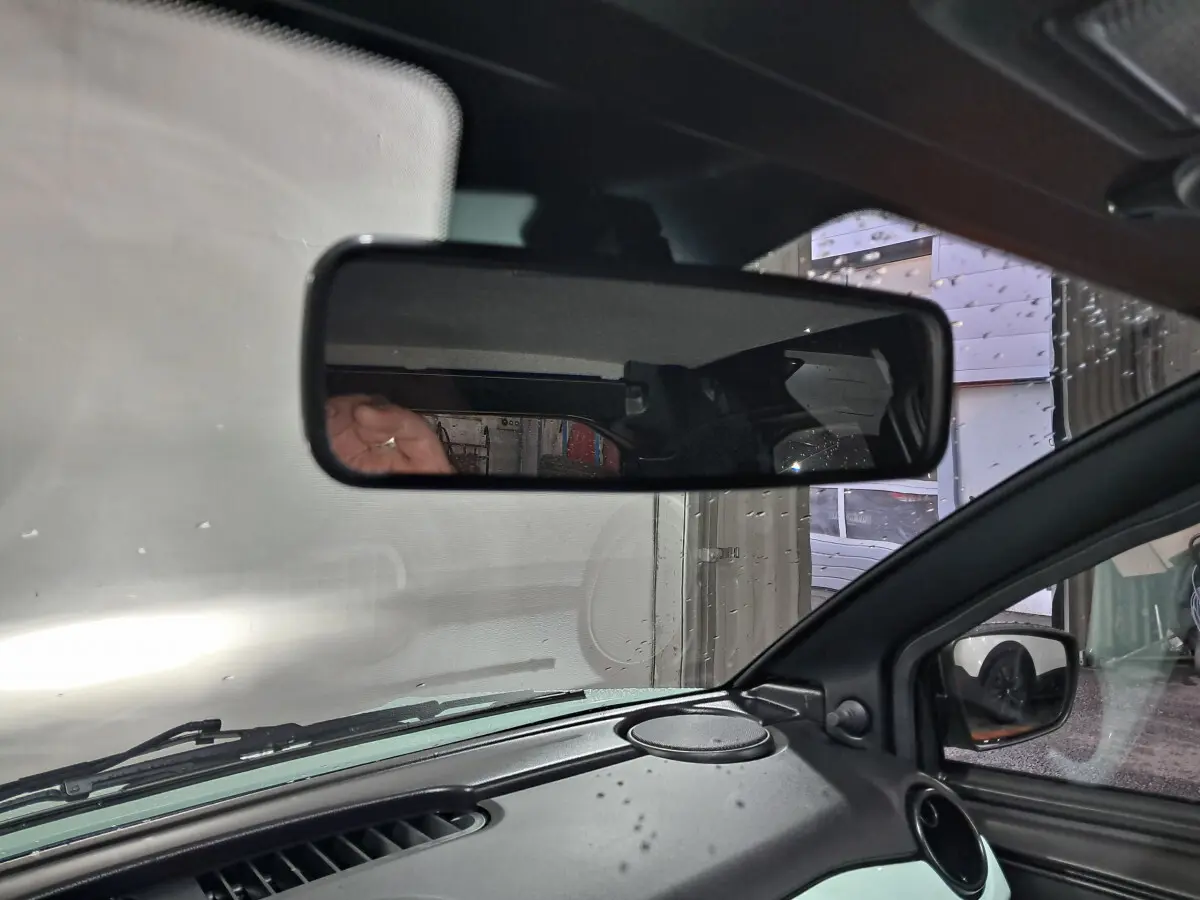 Vue intérieure centrée sur le rétroviseur intérieur d'une Aixam Minauto E chic 2026 vert, avec rétroviseur extérieur caméra côté conducteur visible.