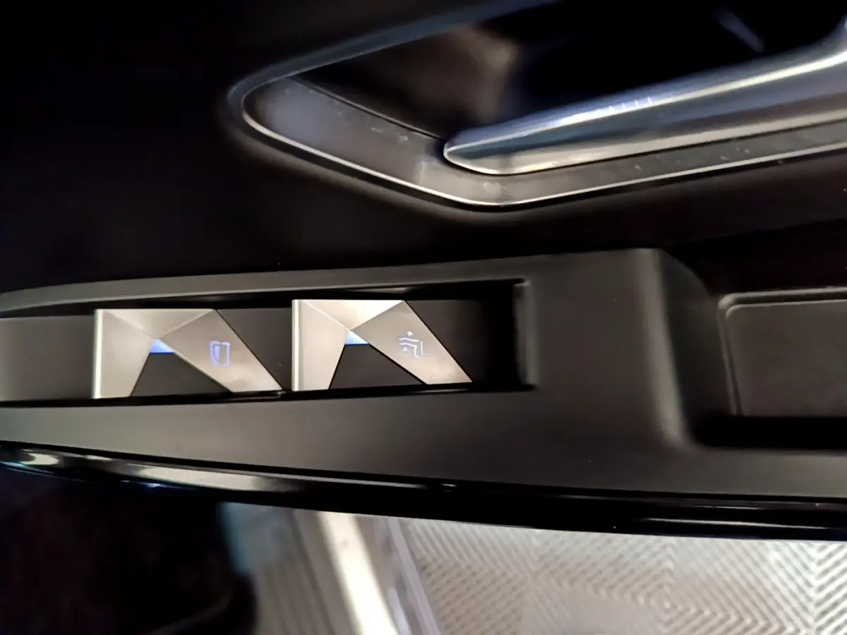Gros plan sur les commandes des vitres électriques côté conducteur du DS7 Crossback gris foncé, avec éclairage bleu.