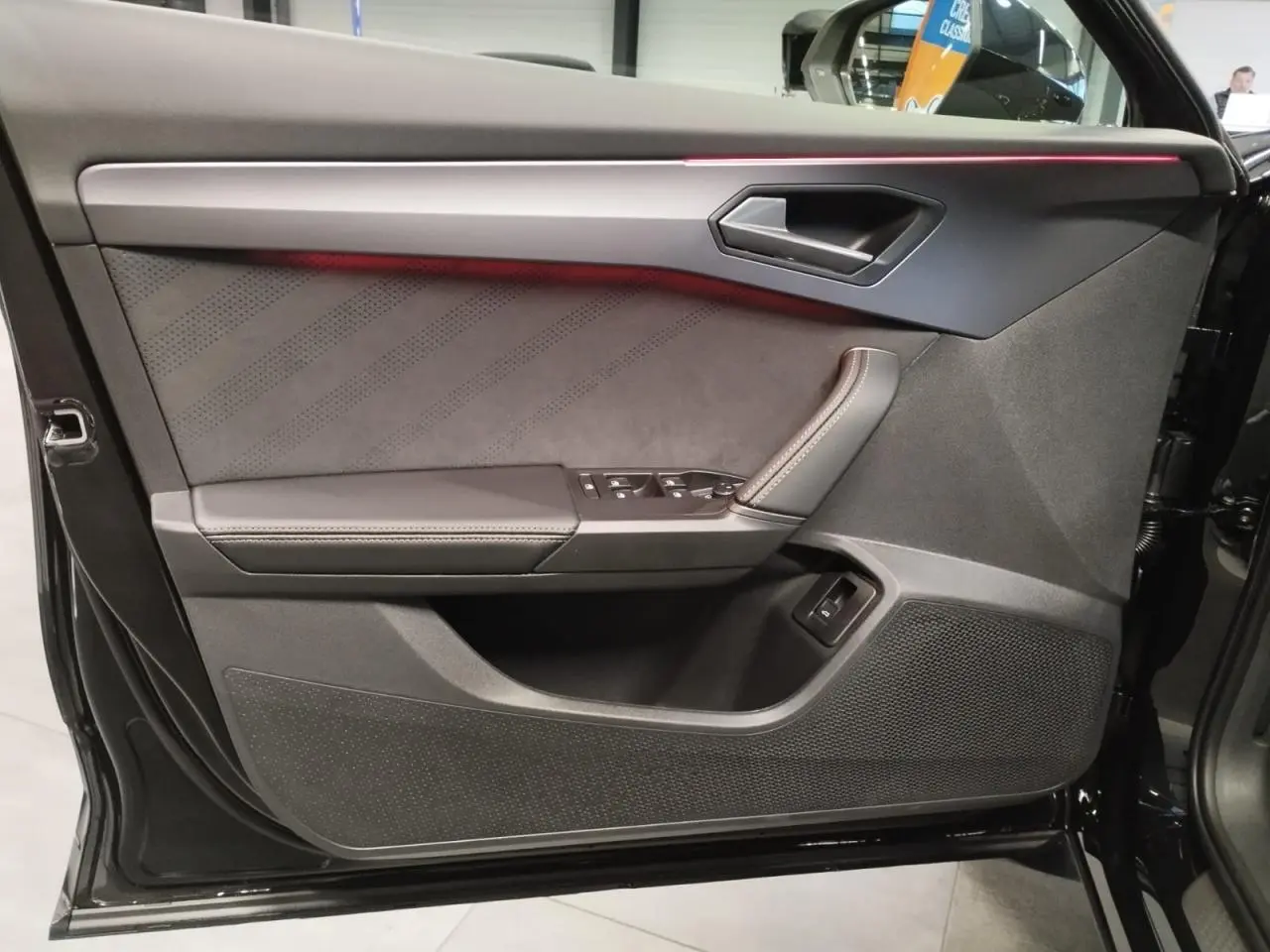 Vue côté gauche de la porte avant noire métal du CUPRA Formentor avec insert suédine et éclairage d'ambiance rouge.