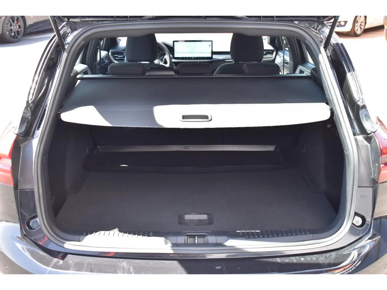 Vue arrière du coffre ouvert d'une Ford Focus SW 2025 Agate Black Metallic, avec cache-bagages déployé et intérieur noir.
