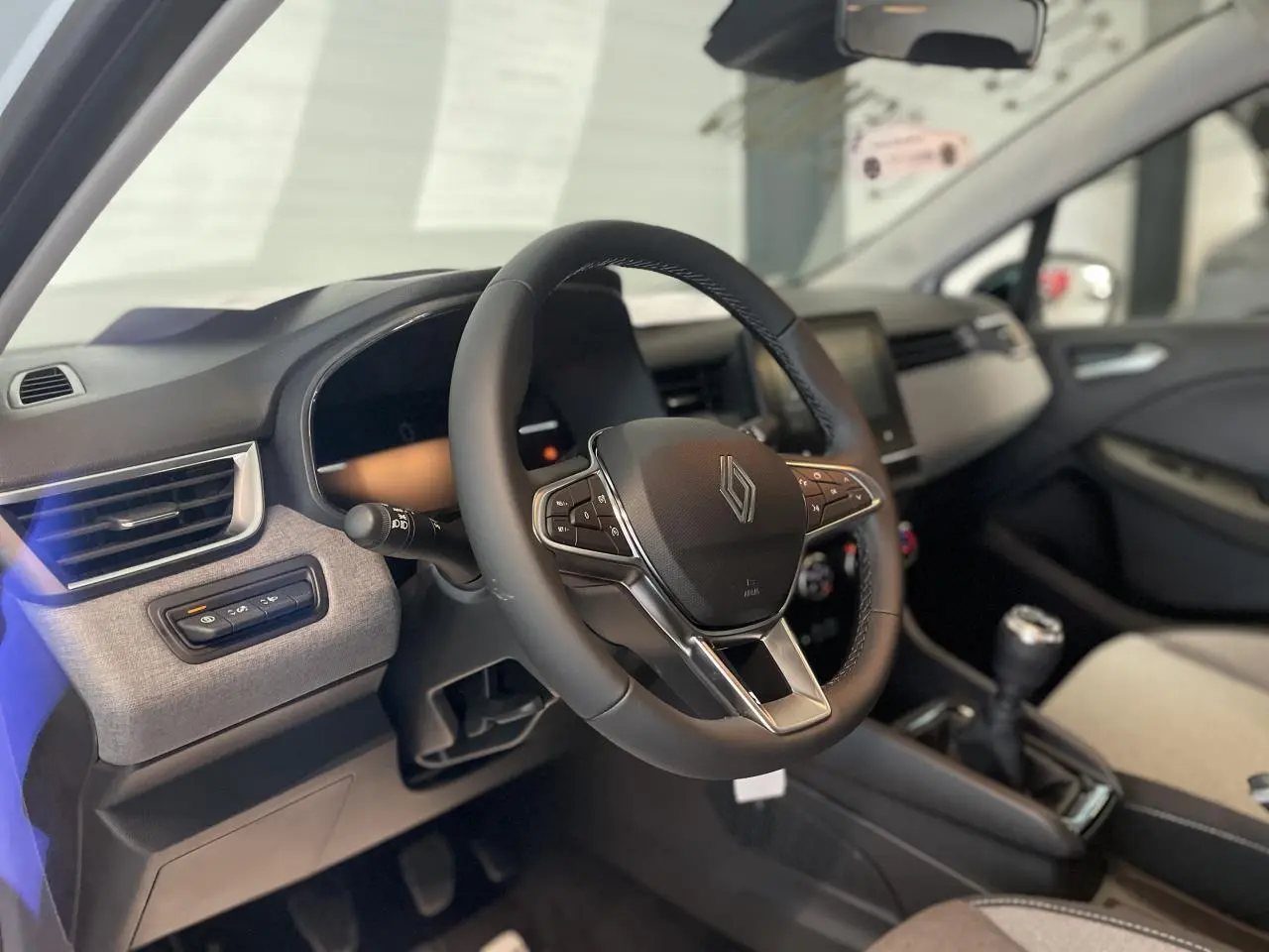 Intérieur Renault Clio 2025 vu côté conducteur, volant multifonction noir et tableau de bord avec inserts gris mozaic.