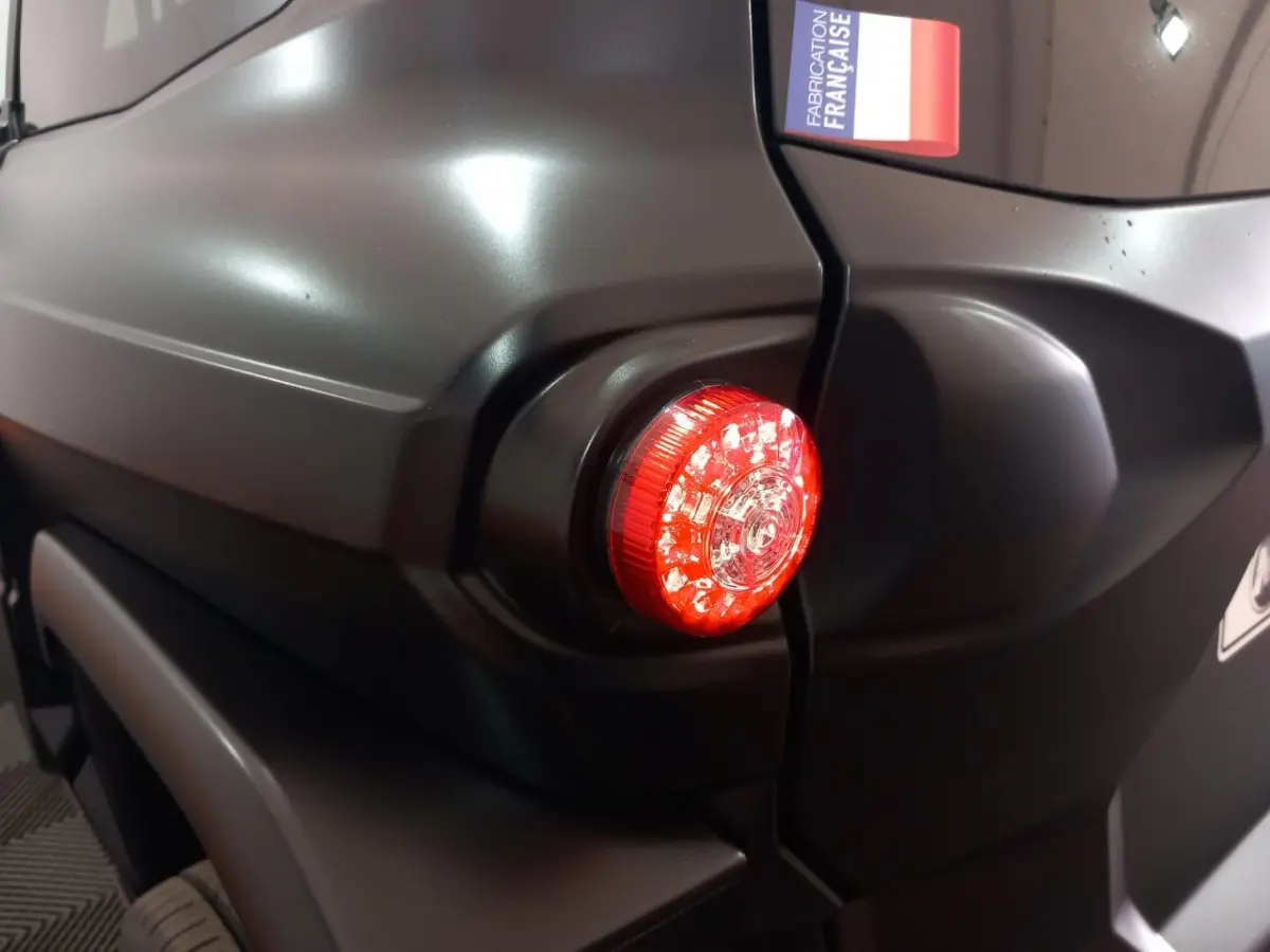 Gros plan sur le feu arrière droit rouge d’une Aixam Mega E-Scouty Evo bleu, avec autocollant "Fabrication Française".