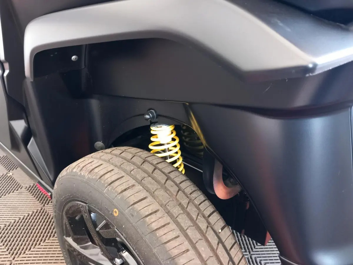 Gros plan sur la suspension arrière avec ressort jaune et roue noire du côté gauche de l'AIXAM MEGA bleu électrique.