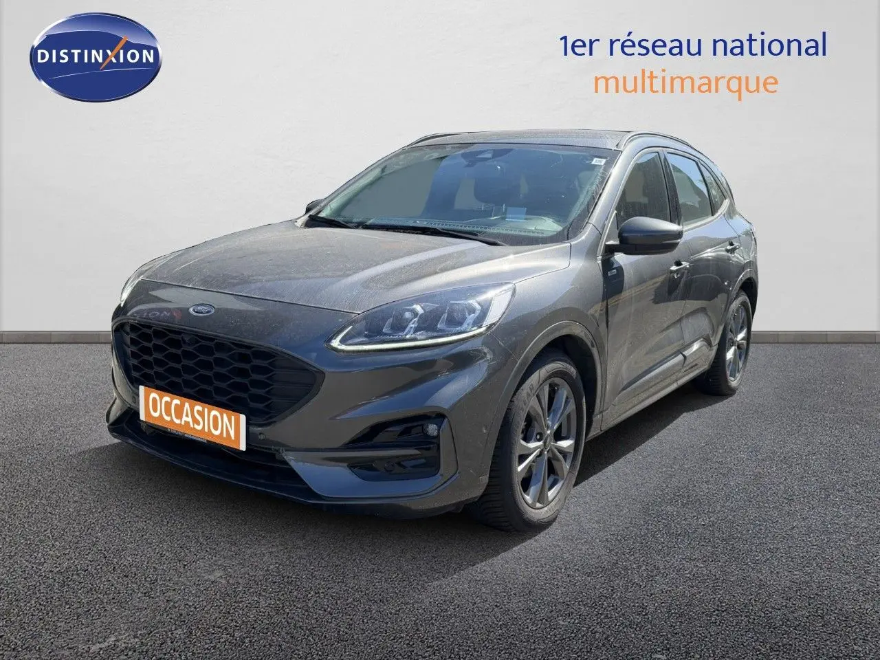 Ford Kuga 2.0D ST-Line gris magnétique métal en 3/4 avant droit sur sol gris, plaque occasion visible.
