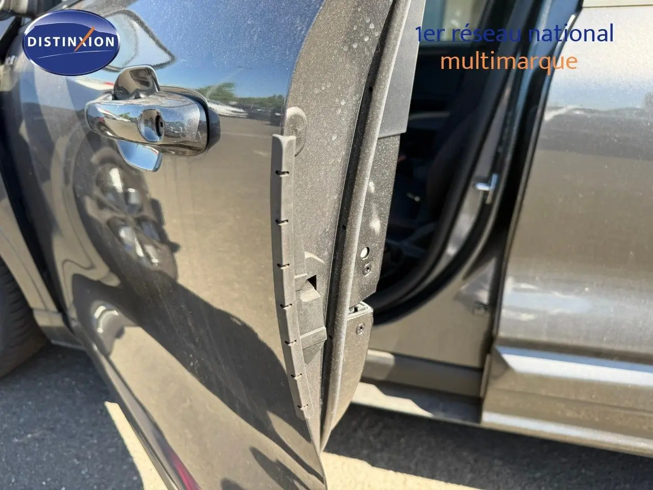 Vue rapprochée de la porte avant gauche ouverte d’un Ford Kuga 2024 gris magnétique métal, avec reflet et poignée chromée.