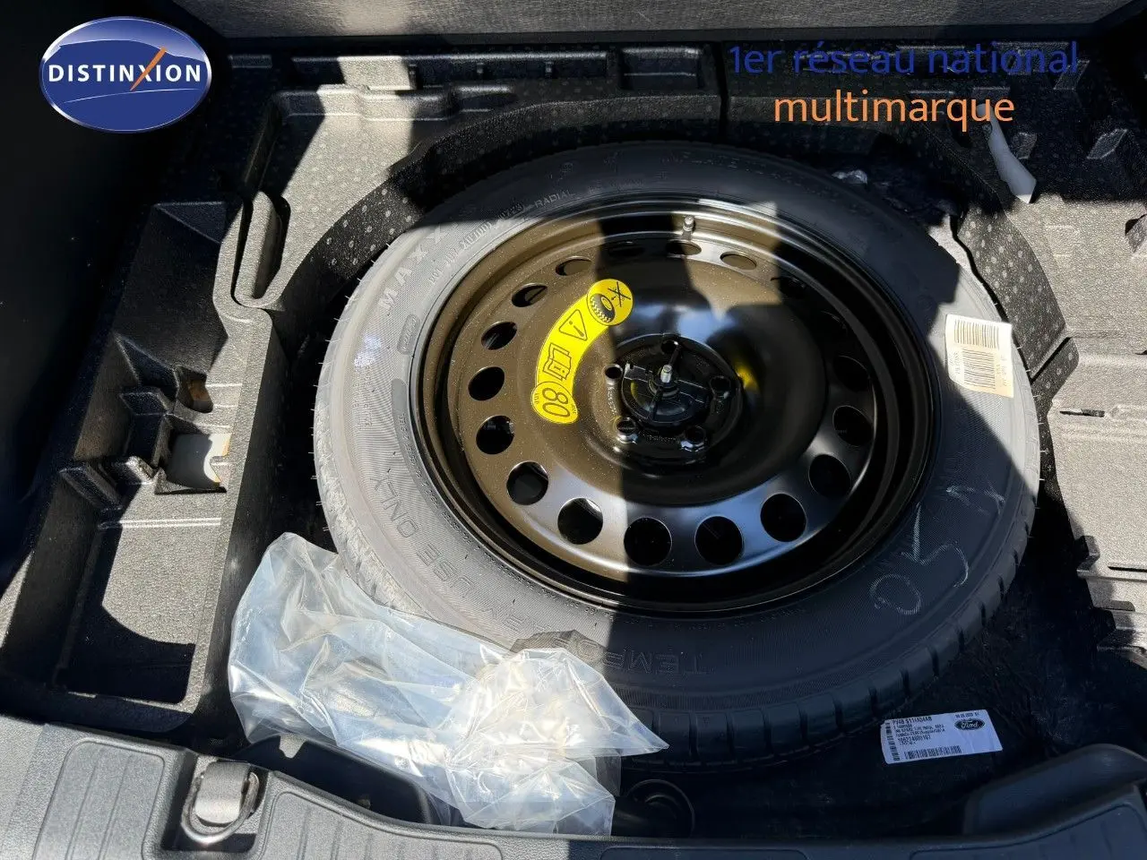 Roue de secours noire dans le coffre d’un Ford Kuga 2024 gris magnétique, avec kit de réparation plastique à côté.