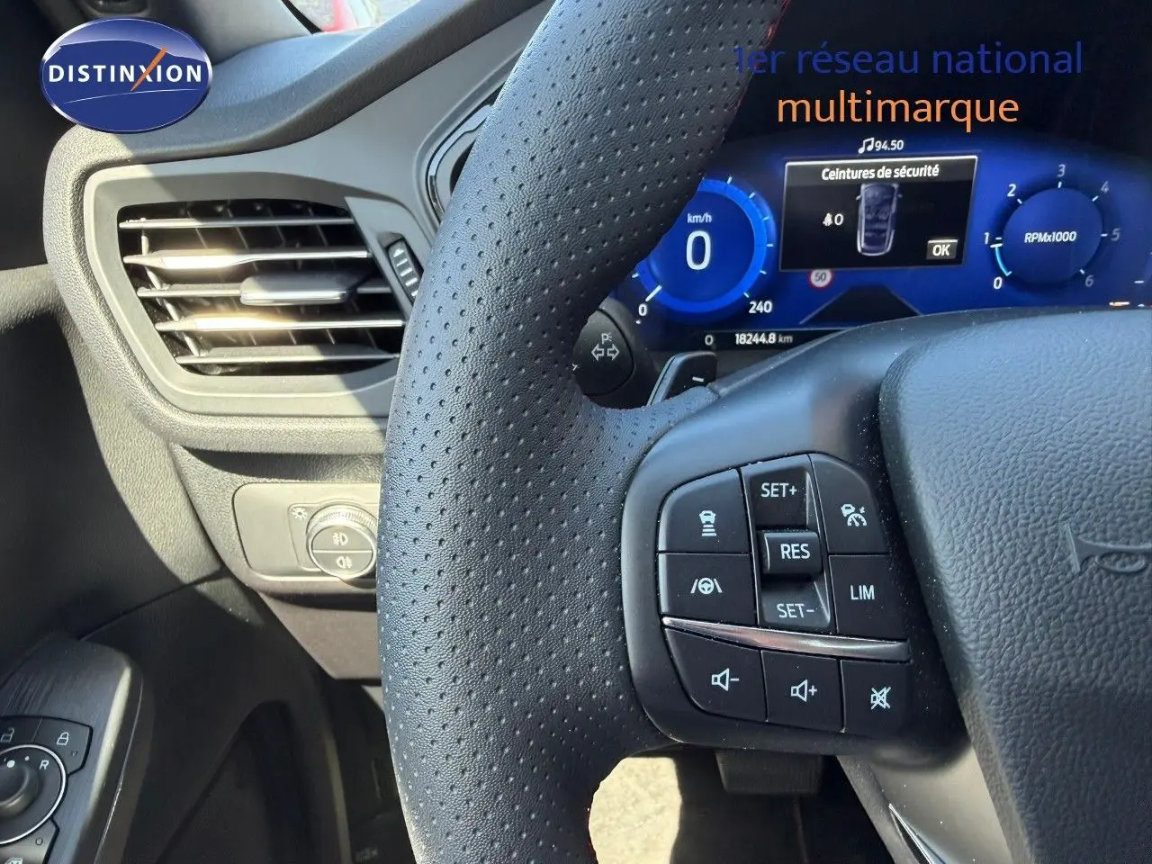 Vue rapprochée du volant perforé et du tableau de bord numérique bleu d’un Ford Kuga 2024 gris magnétique.