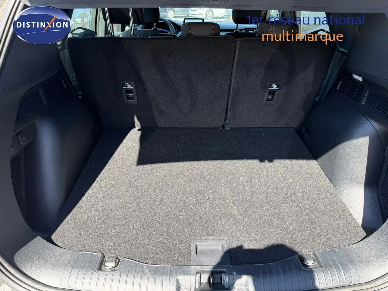 Coffre ouvert du Ford Kuga 2024 gris magnétique, vue arrière montrant l’espace de chargement et les dossiers de sièges noirs.