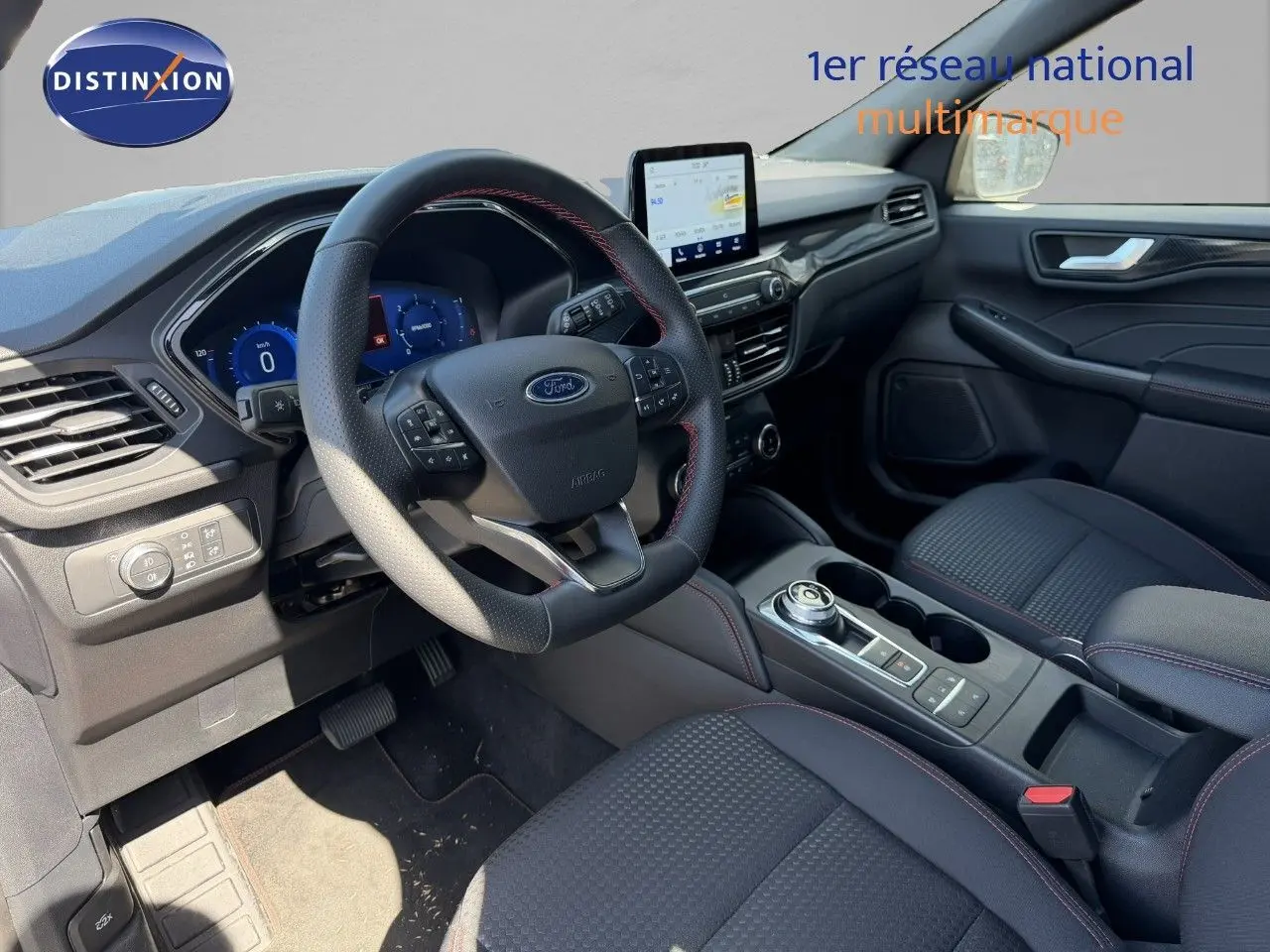 Intérieur Ford Kuga 2024 vue côté conducteur, volant cuir noir avec surpiqûres rouges et écran tactile central.