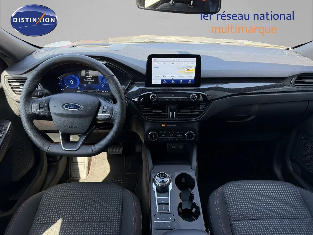 Vue intérieure du tableau de bord et volant du Ford Kuga 2024, avec écran tactile et sellerie tissu gris.