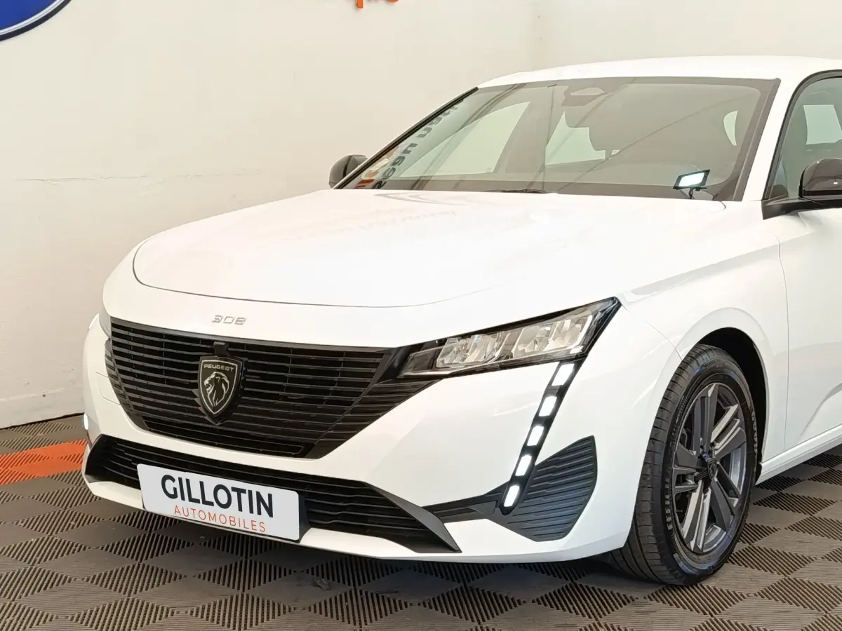 Peugeot 308 blanc vue 3/4 avant droit, avec calandre noire et feux LED verticaux distinctifs.