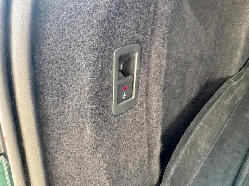 Détail de la commande de rabattement de siège arrière sur la moquette noire du coffre d'une Audi S4 Avant Vert Gotland.