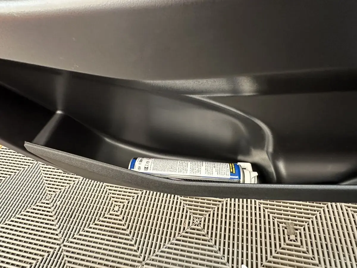 Gros plan sur le rangement intérieur noir d'une Aixam Ambition 0.5 City Pack blanc, avec une bombe aérosol posée.