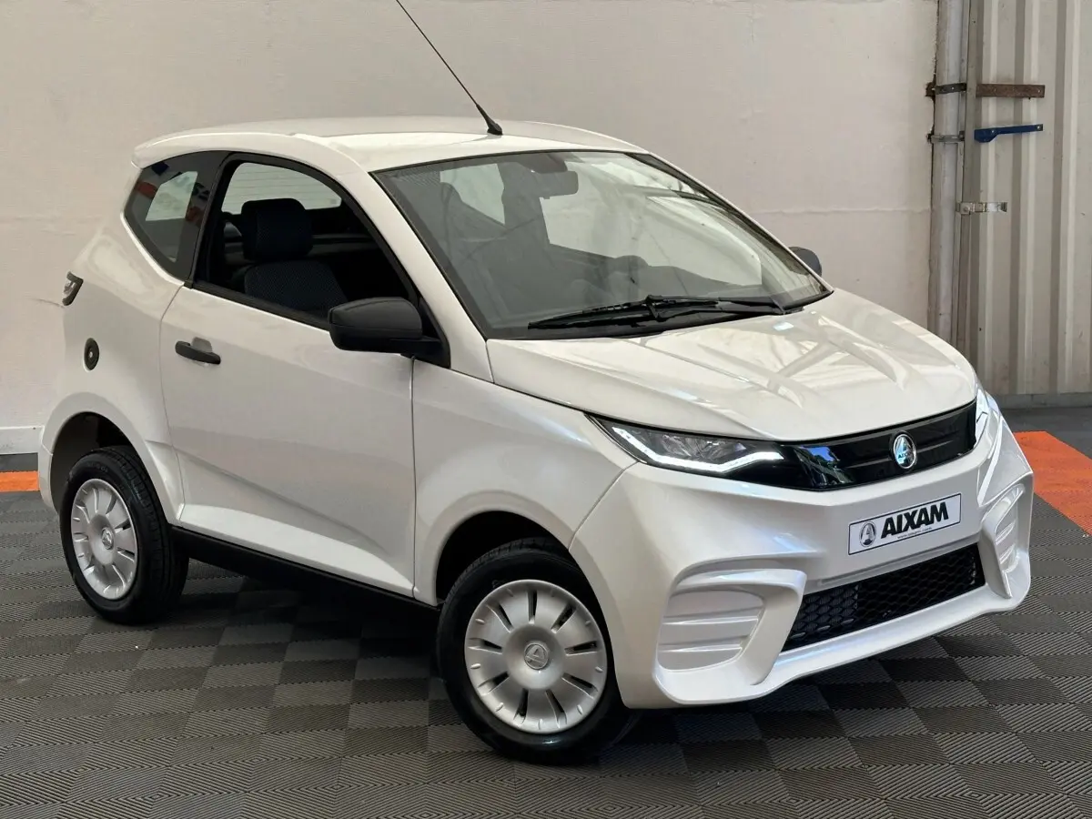 Vue 3/4 avant d'une Aixam Ambition 0.5 City Pack blanche avec rétroviseur caméra côté gauche visible.