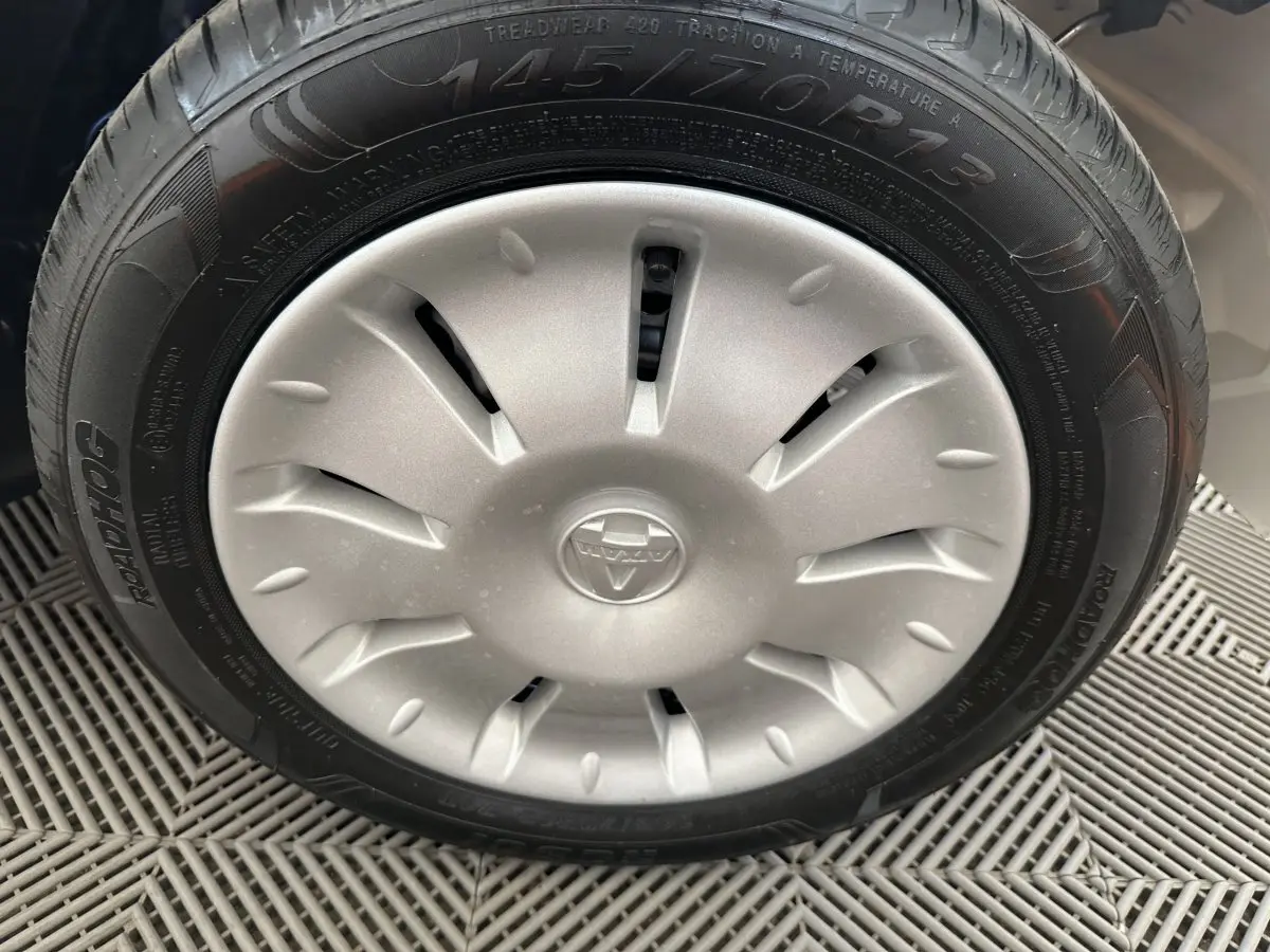 Gros plan sur la roue avant droite de l'AIXAM AMBITION 0.5 CITY PACK blanche, avec enjoliveur argenté et logo central.