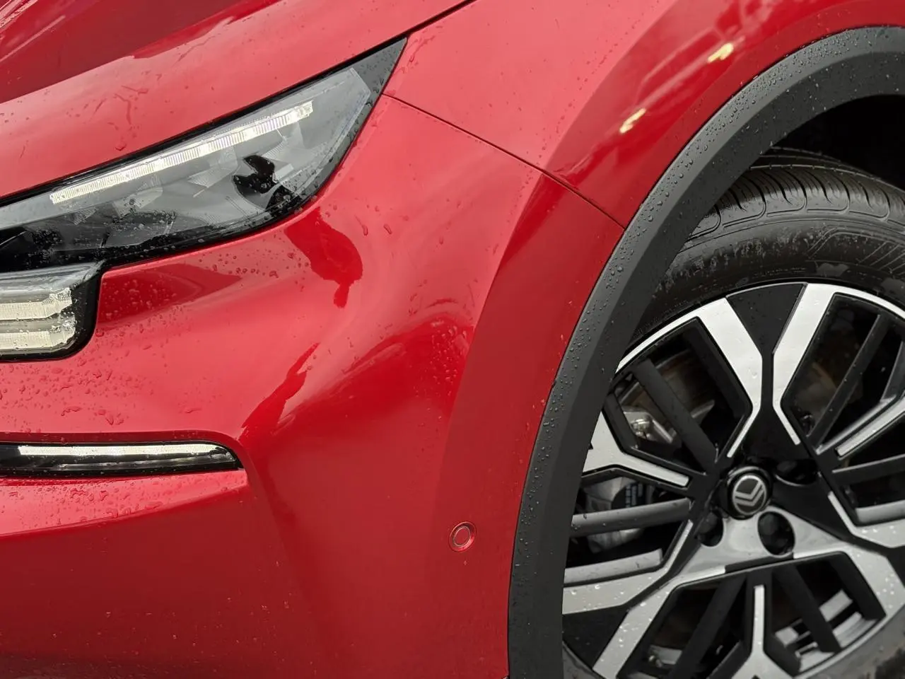 Gros plan sur l'avant droit de la Citroën C4 Hybrid 145 rouge Elixir, mettant en valeur le phare LED et la jante alliage 18 pouces.