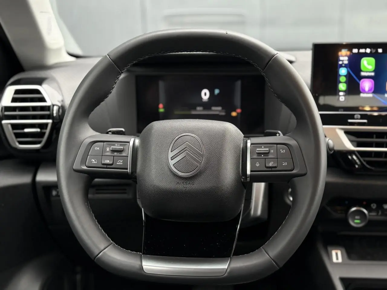Vue rapprochée du volant cuir noir du Citroën C4 Hybrid 2025 avec commandes intégrées et tableau de bord numérique.