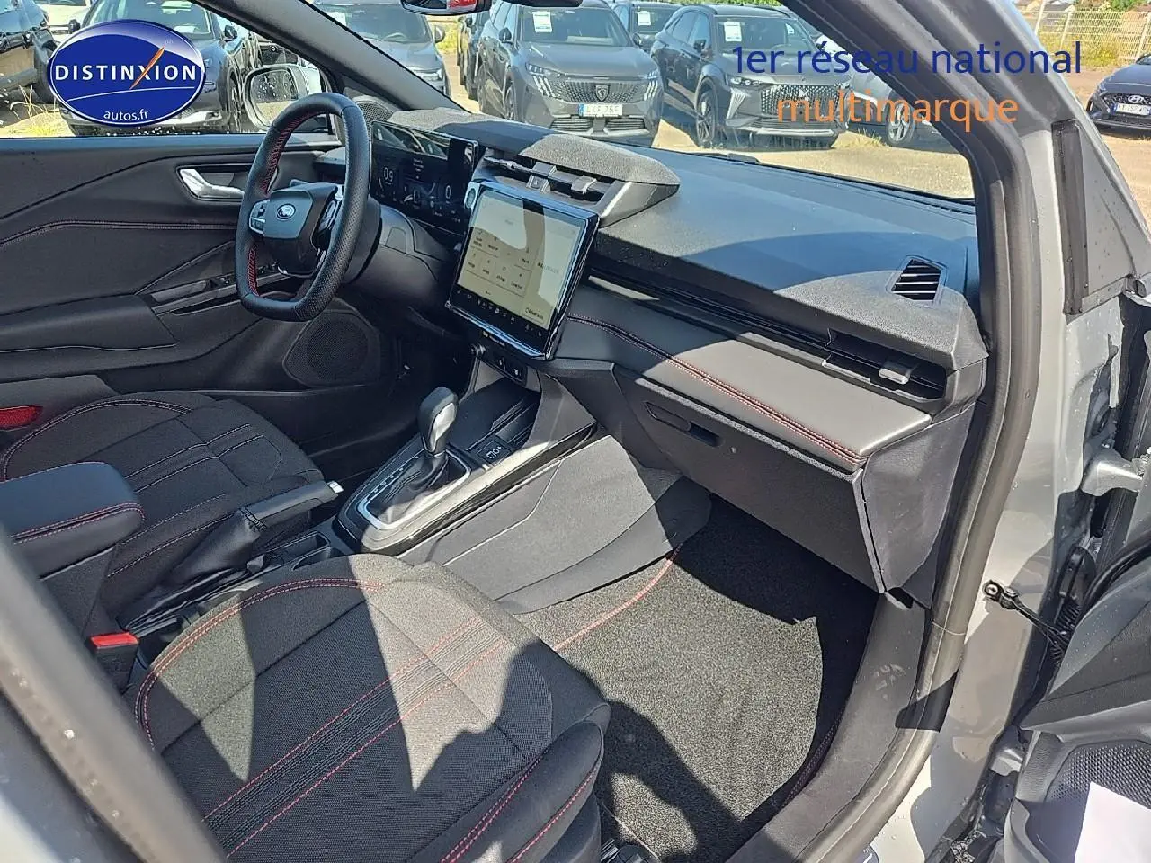 Intérieur avant droit du Ford Puma gris cactus 2025, avec sièges tissu noir et surpiqûres rouges, écran tactile central visible.