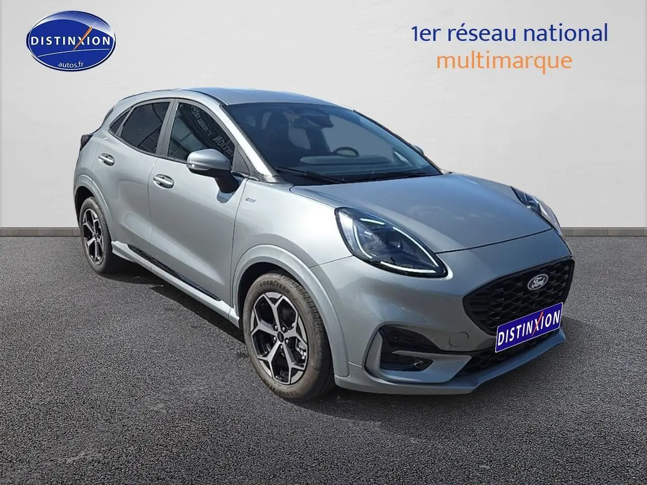 Ford Puma gris cactus en 3/4 avant droit avec jantes 17 pouces et phares LED allumés sur fond neutre.
