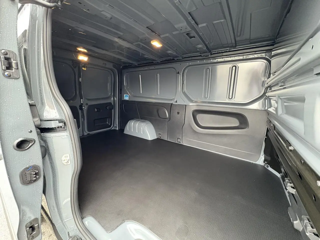Intérieur du fourgon Renault Trafic L2H1 2025 gris urbain, vue de la zone de chargement avec plancher antidérapant noir.
