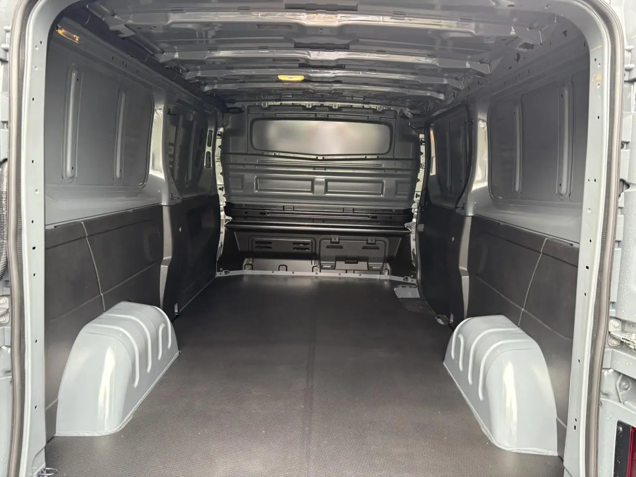 Vue intérieure arrière du Renault Trafic Fourgon gris urbain avec plancher antidérapant et cloison tôlée complète.