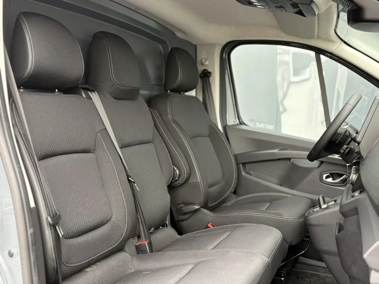 Vue intérieure côté droit du Renault Trafic Fourgon 2025, sièges noirs avec coutures blanches et plancher antidérapant.