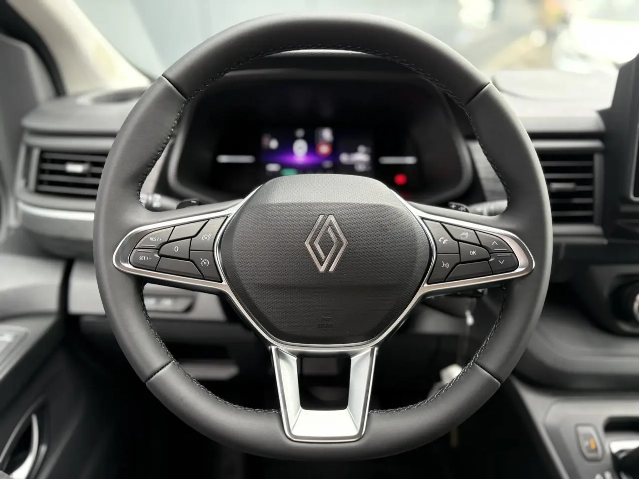 Vue rapprochée du volant en cuir multifonction du Renault Trafic Fourgon 2025, avec commandes intégrées et tableau de bord numérique flou.