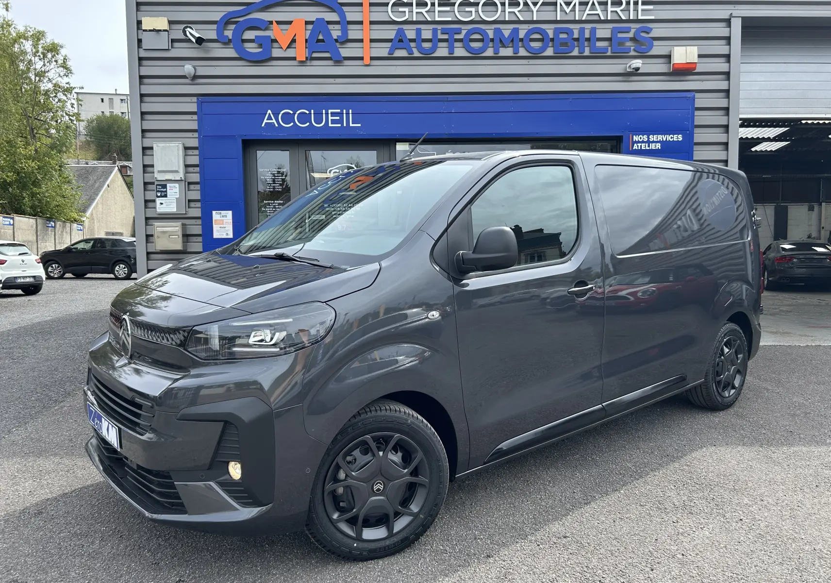 Citroën Jumpy gris titane en 3/4 avant droit, avec jantes noires et calandre moderne devant un garage GMA.