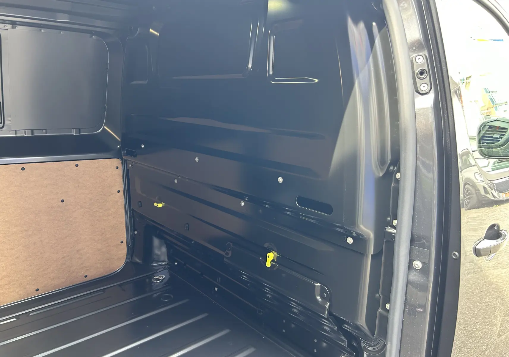 Vue intérieure côté droit de la zone de chargement du Citroën Jumpy gris titane, montrant la paroi métallique et panneau bois.