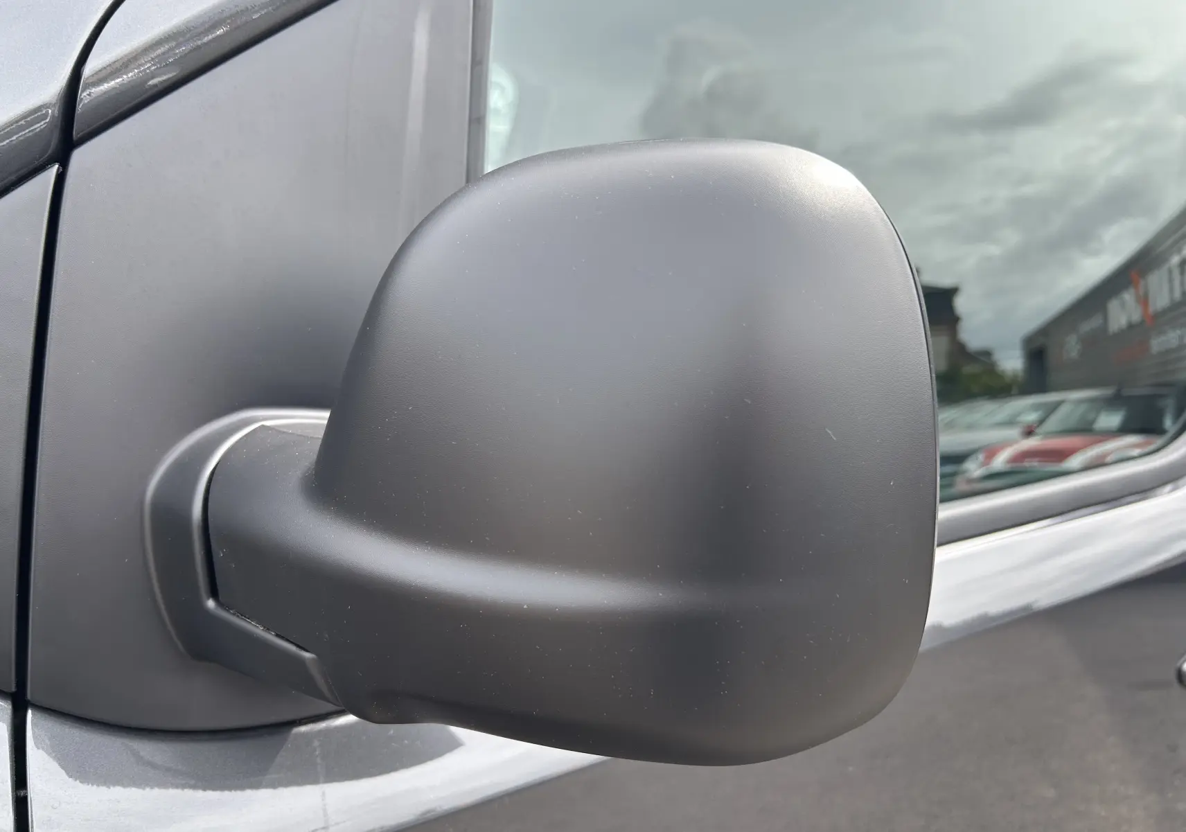 Rétroviseur côté gauche en gros plan du Citroën Jumpy gris titane sous un ciel nuageux.