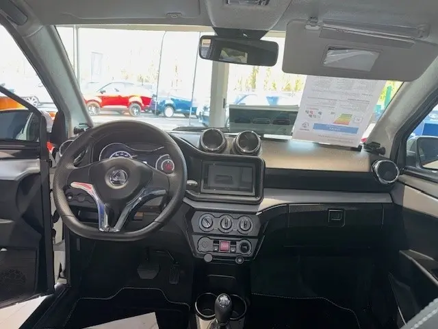 Vue intérieure avant de l'AIXAM AMBITION 0.5 CROSSOVER PREMIUM blanc, tableau de bord avec écran central et volant trois branches.