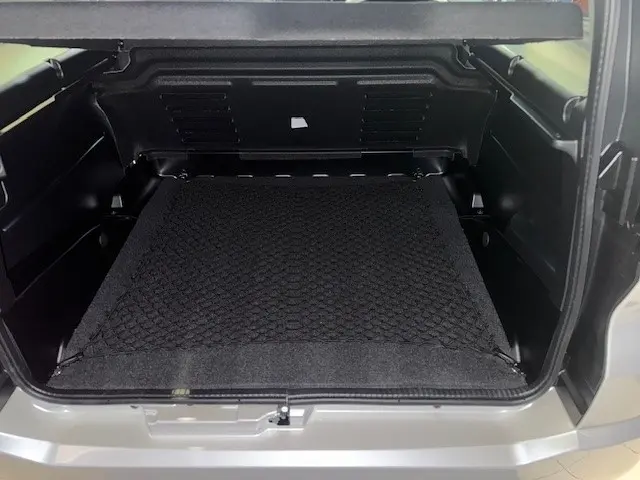 Vue intérieure du coffre ouvert de l'AIXAM AMBITION 0.5 CROSSOVER PREMIUM blanc, montrant l'espace de rangement avec filet de sécurité.