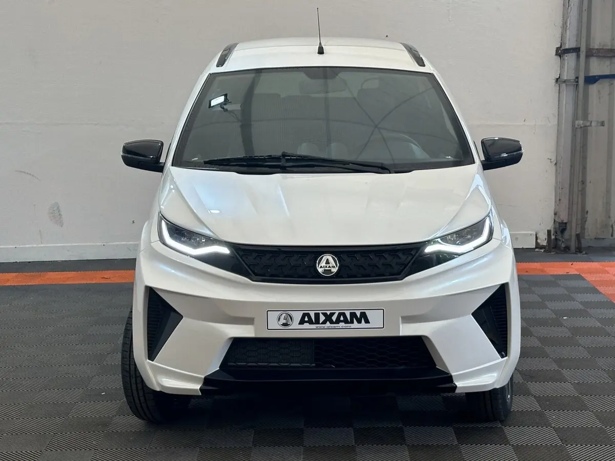 Vue frontale d'une Aixam Ambition 0.5 Crossover Premium blanche avec calandre noire et rétroviseurs caméra côté gauche.