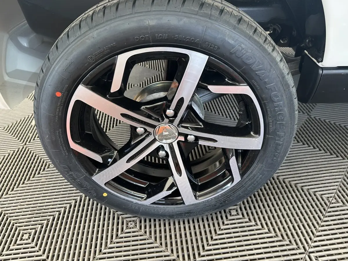 Gros plan sur la roue avant droite d’une Aixam Ambition 0.5 Crossover Premium blanche avec jante noire et argentée.