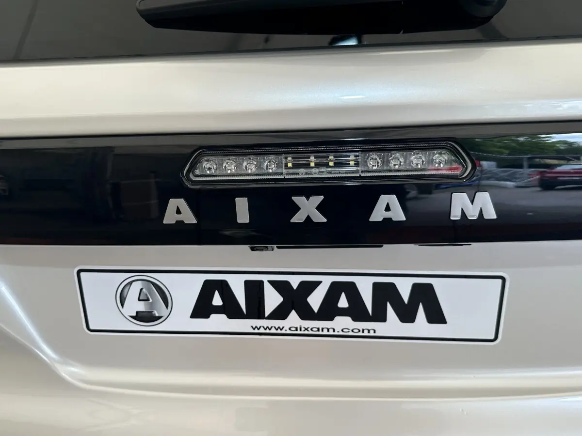 Gros plan arrière sur le logo AIXAM en lettres argentées sur fond noir, carrosserie blanche brillante.