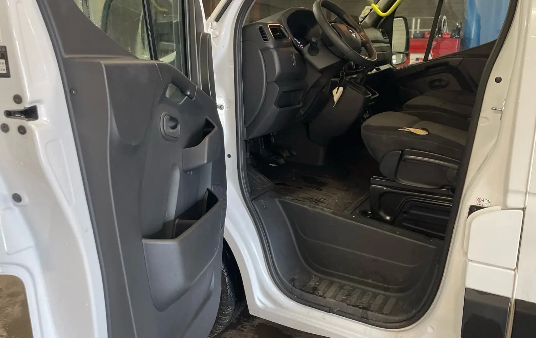 Vue intérieure côté conducteur du Renault Master blanc 2020, montrant l'ouverture de porte et les sièges noirs.