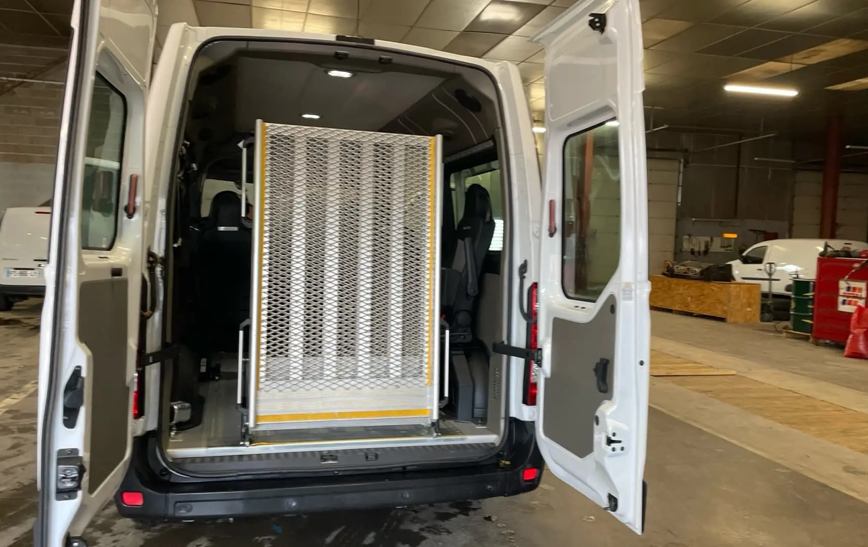 Vue arrière du Renault Master blanc 2020 avec portes ouvertes et rampe d'accès pour fauteuil roulant déployée.
