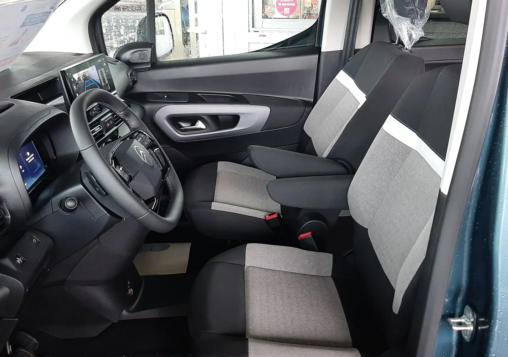 Vue intérieure côté conducteur du Citroën Berlingo bleu Kiama, montrant les sièges tissu gris et noir et le tableau de bord moderne.