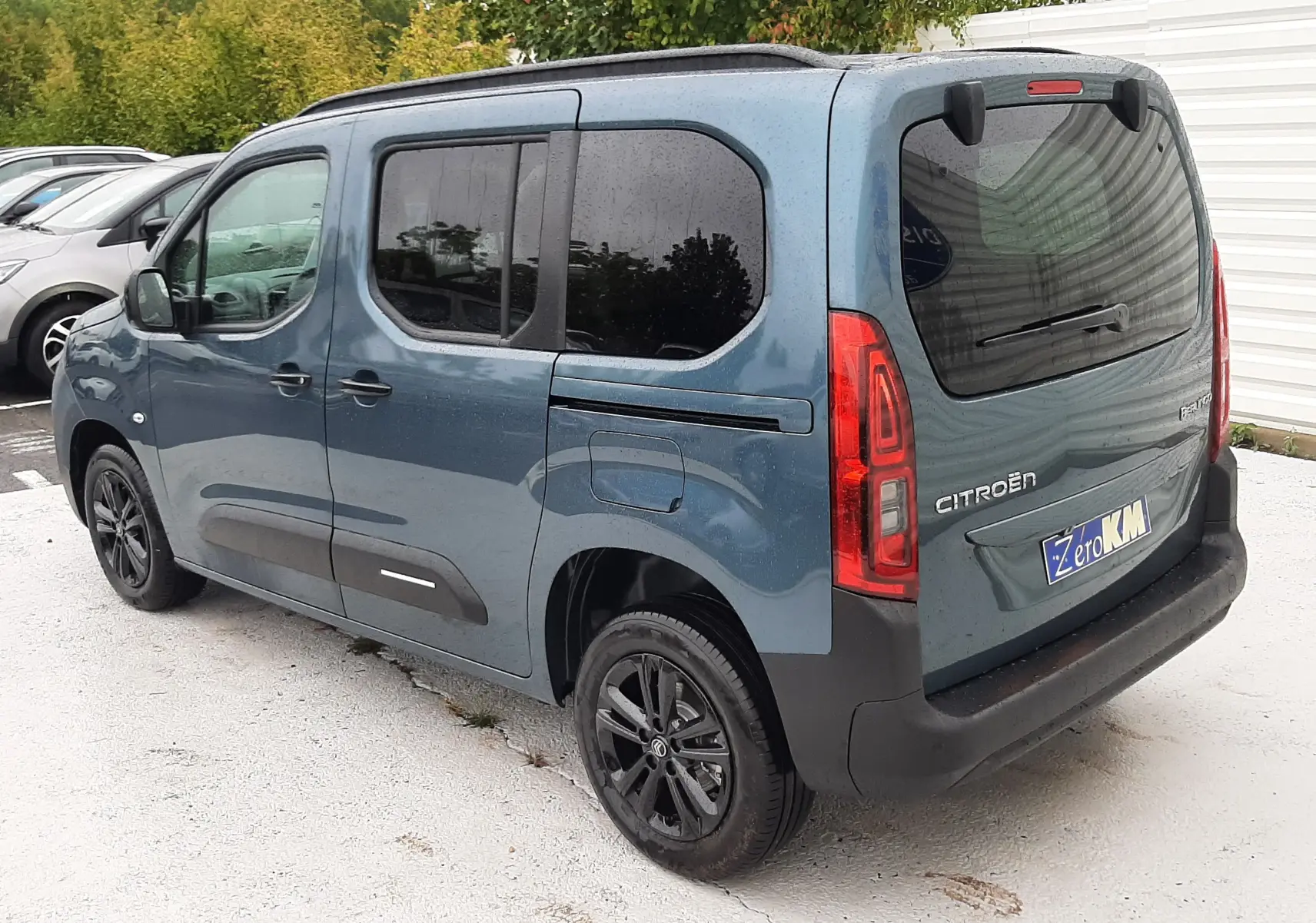 Vue 3/4 arrière droite d'un Citroën Berlingo bleu Kiama avec vitres teintées et jantes noires, stationné en extérieur.