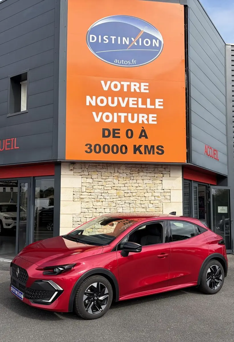 Renault Clio Evolution rouge vue en 3/4 avant droit, avec jantes noires et calandre distinctive, devant un bâtiment commercial.